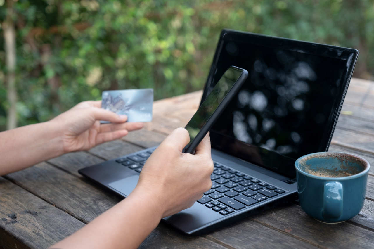 Smartphone and credit cards in hand with laptop and coffee