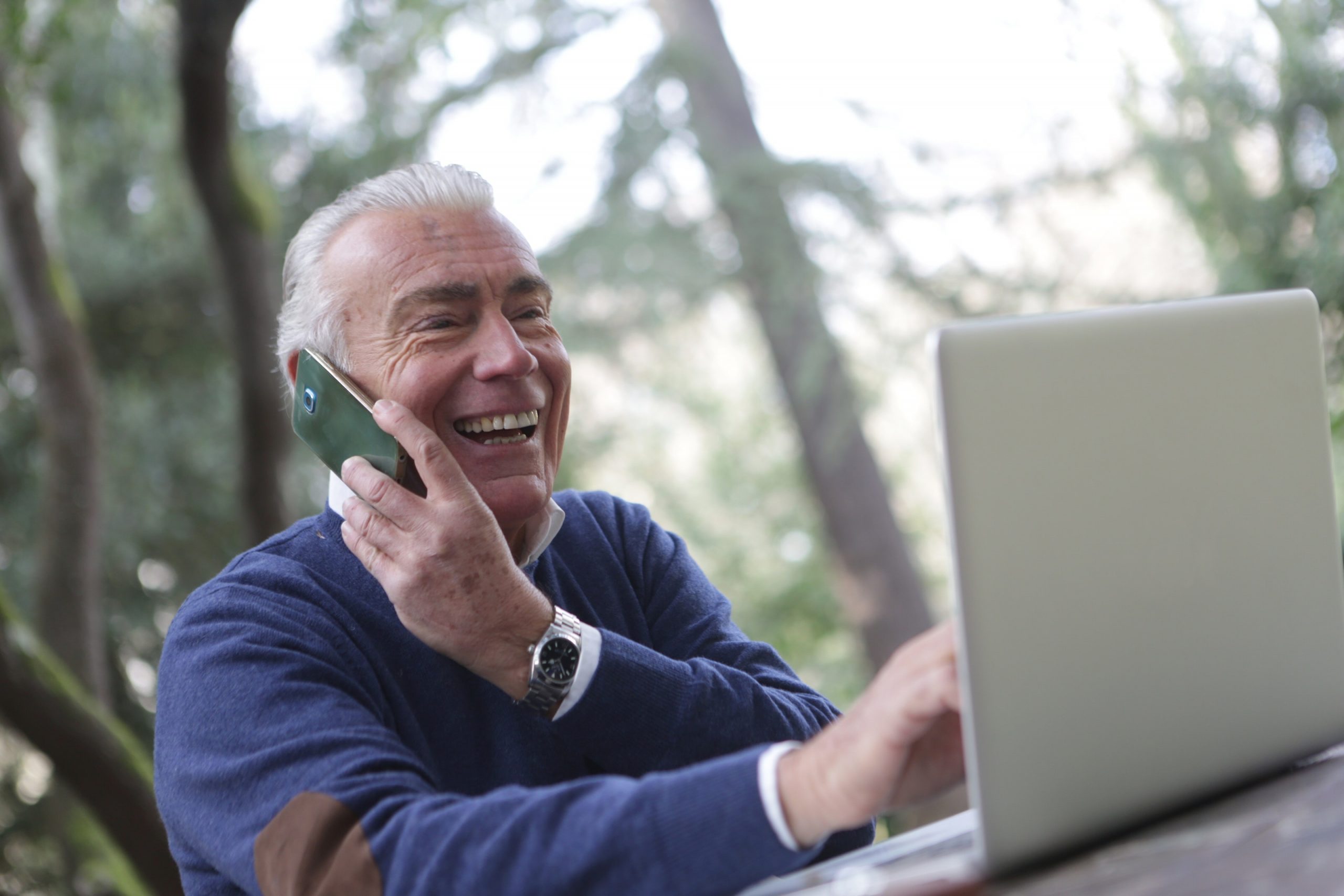 happy old man calling on mobile while using his laptop